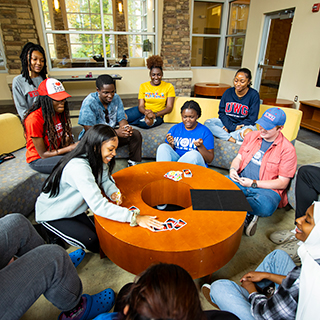 Eleven students around a table playing uno. 