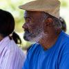 African American man with a beard wearing a blue shirt and tan flat cap.