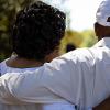 Man and woman, both wearing white, standing with their backs to the camera with their arms around each other.