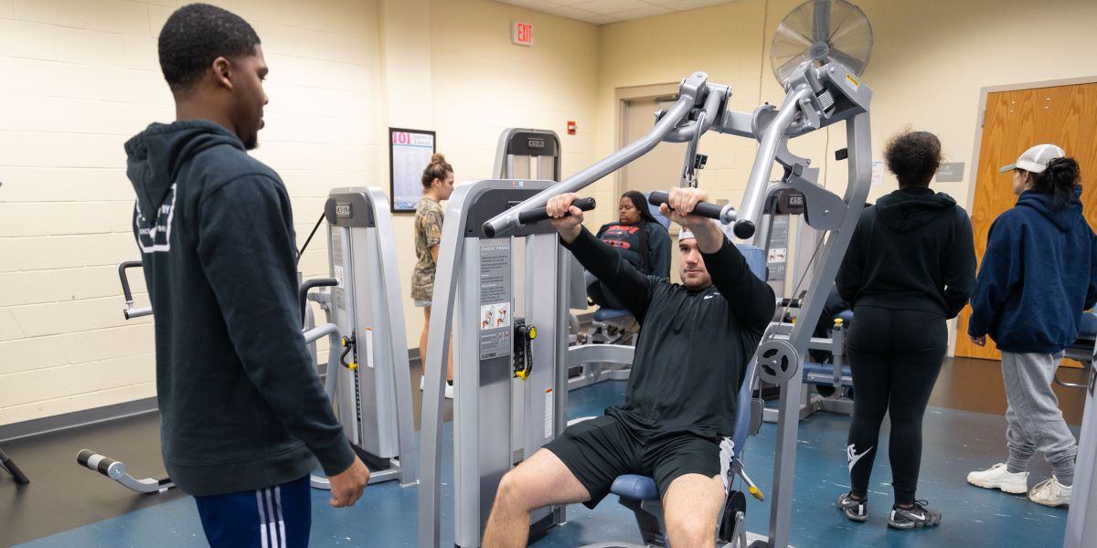 Students using a workout machine in the gym