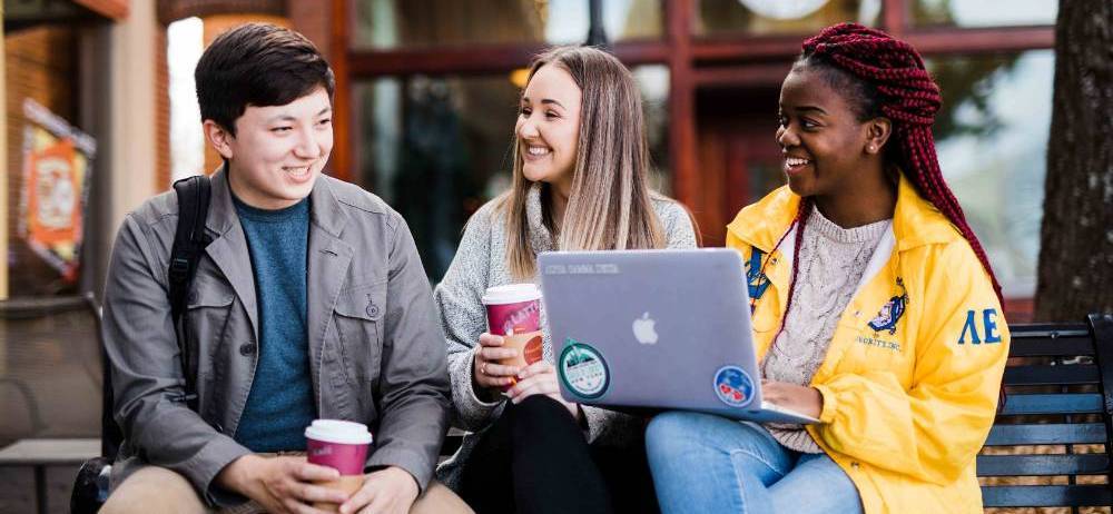 People on laptop together talking outside.