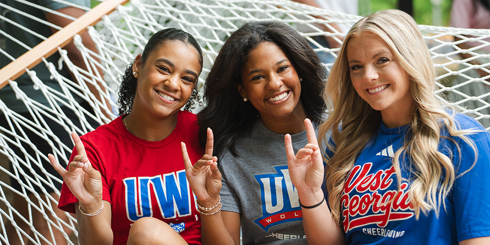 Three female students throw up a UWG hand sign in a hammock.