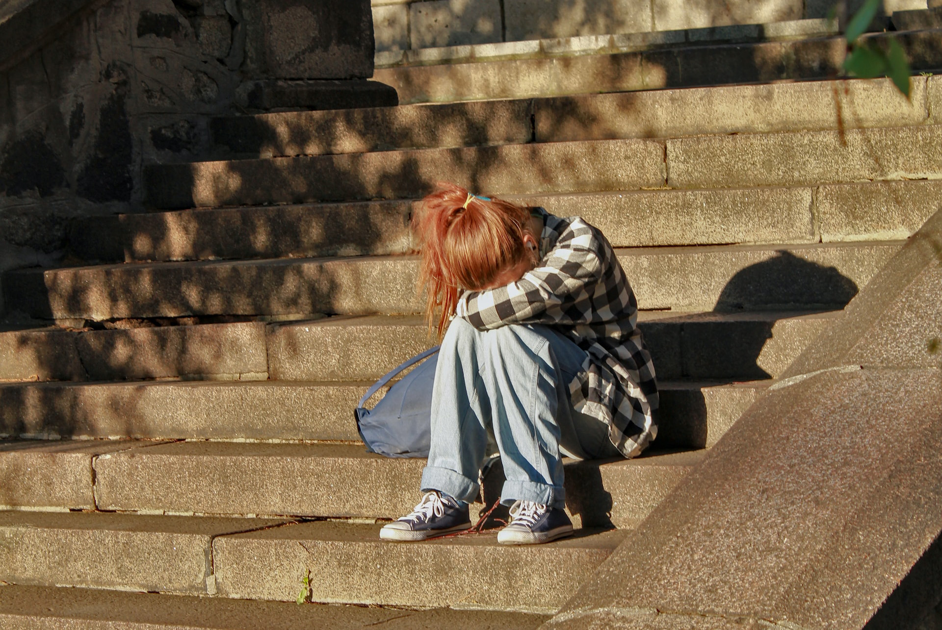 woman in black and white checkered top sitting on concrete stairs with her head down