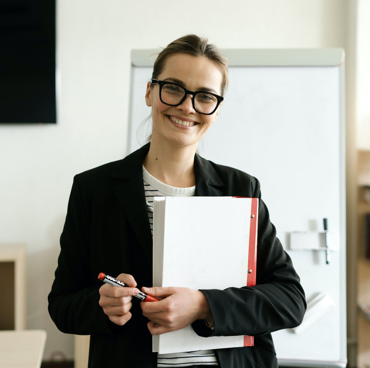 A female teacher holding a red marker and a folder