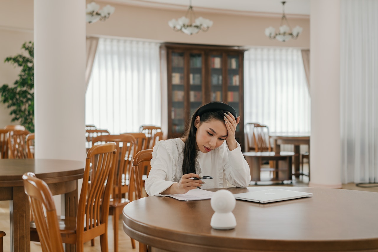 A Woman in White Long Sleeves Looking at the Paper on the Table with Her Hand on Her Head