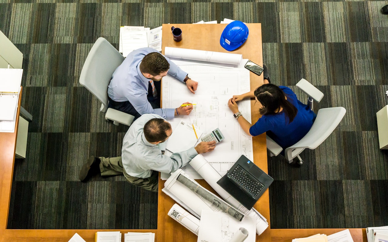 Three People Sitting at a Table looking at blueprints