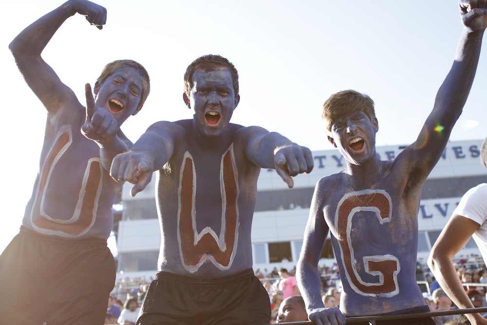 three male students at a football game with U, W, and, G painted on their torsos