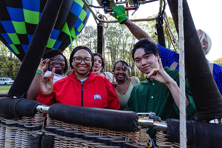 Students in hot air balloon with wolfie hand signs
