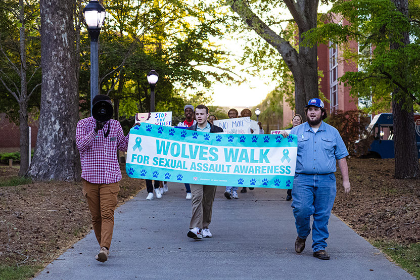Students with a banner that says "wolves walk for sexual assault awareness"