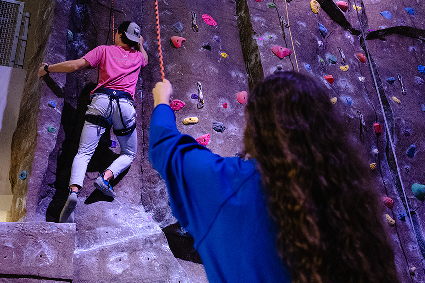 students climbing rock wall and getting belayed by staff