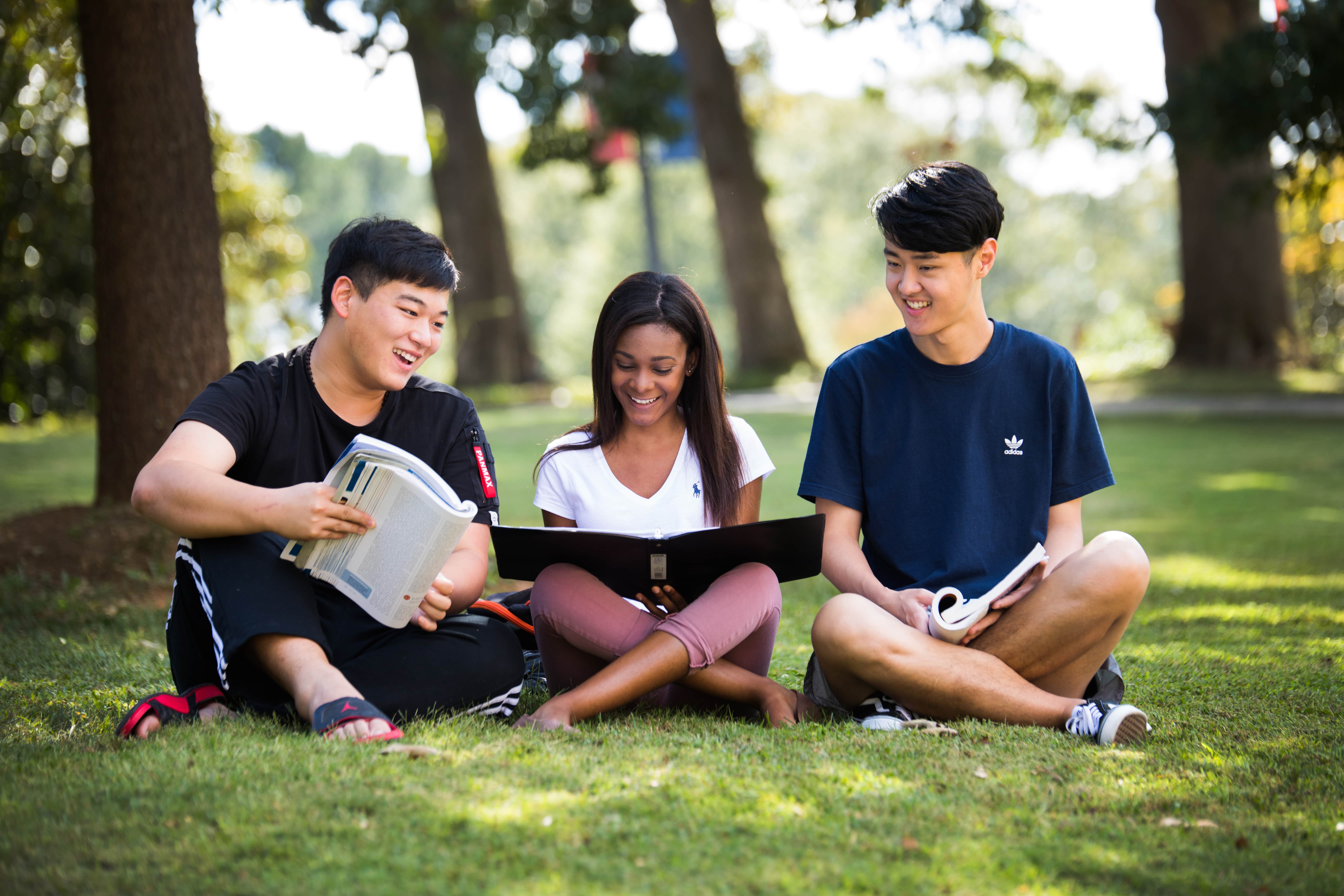 Three students sitting outside college of business reading together.