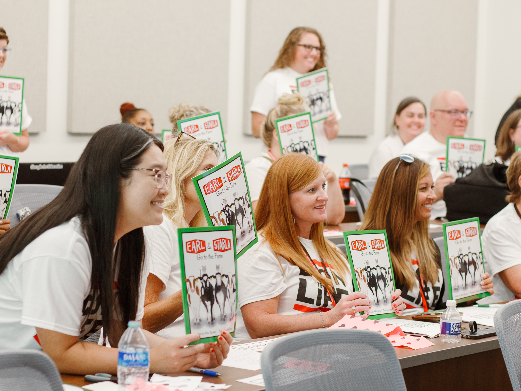 Students holding up flyers in a classroom as they learn to become teachers.