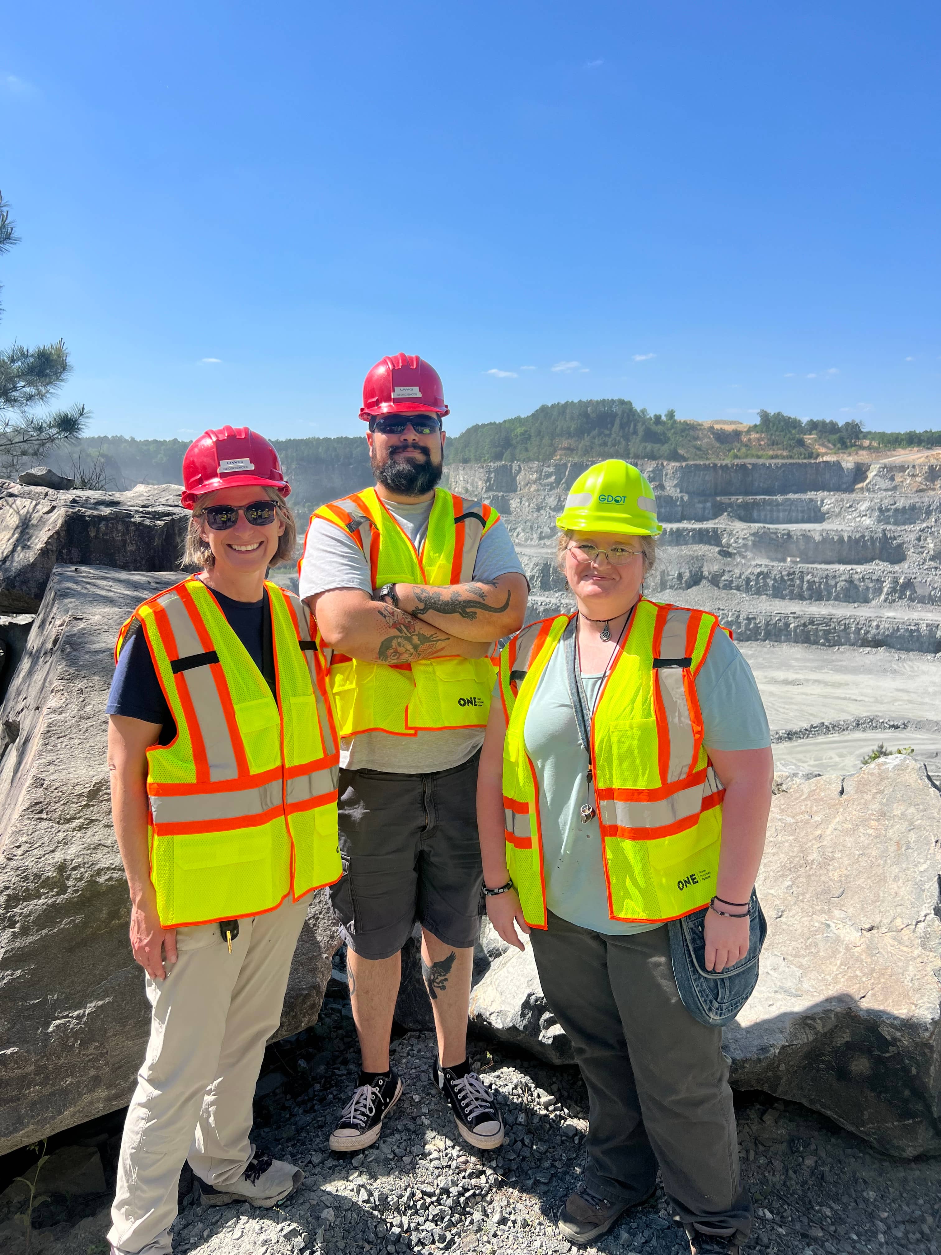 Staff member Randa Harris and two students wearing safety vests and hard hats stand at an overlook above a large quarry during a field learning experience.
