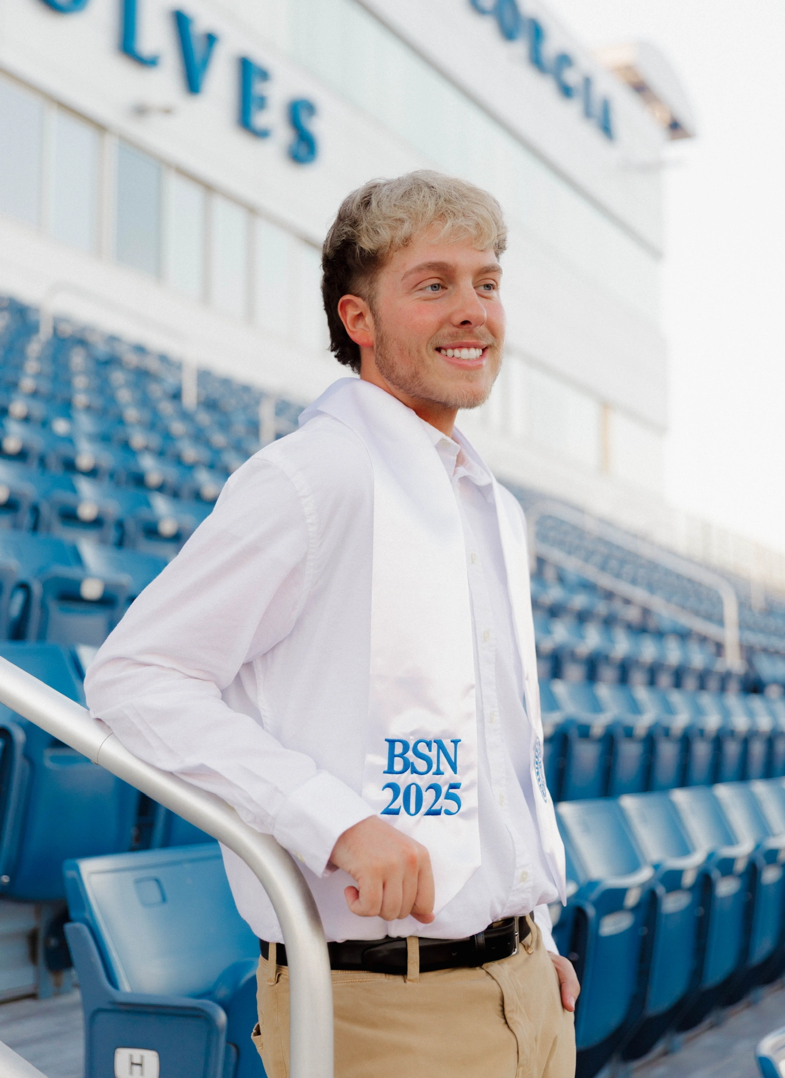 Justin standing in the stadium wearing a BSN stole around his neck, in a white button down and khakis, looking out to the field.
