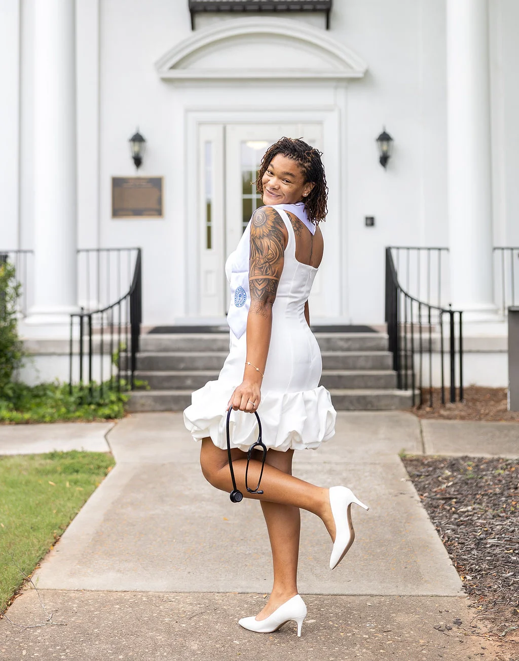 Jaden wearing a white dress and holding a stethoscope outside UWG Newnan.