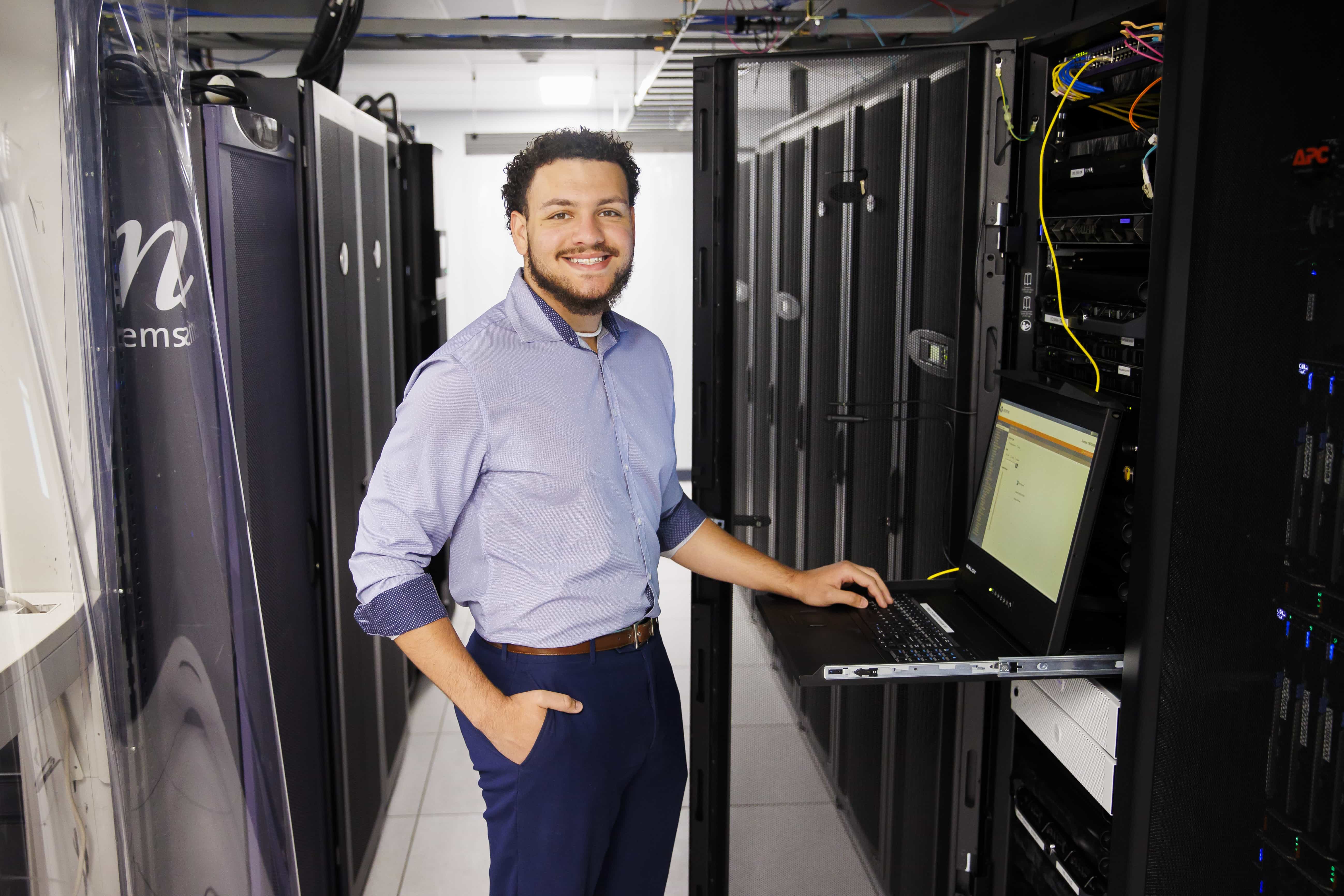 Student standing in server room smiling.