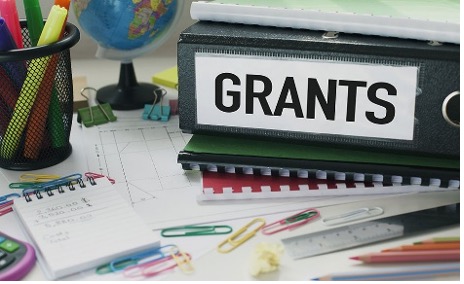 Bind labeled "Grants" sitting on a table with office supplies laying around the desk.