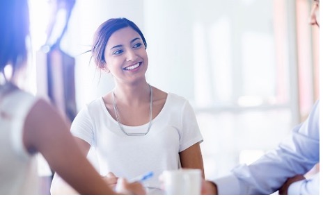 Woman in a white tshirt sitting and smilling at two other individuals with their backs to the camera.