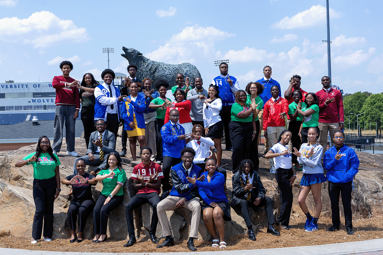 NPHC members doing their organization signs at the wolf statue wearing their various colors and greek letters