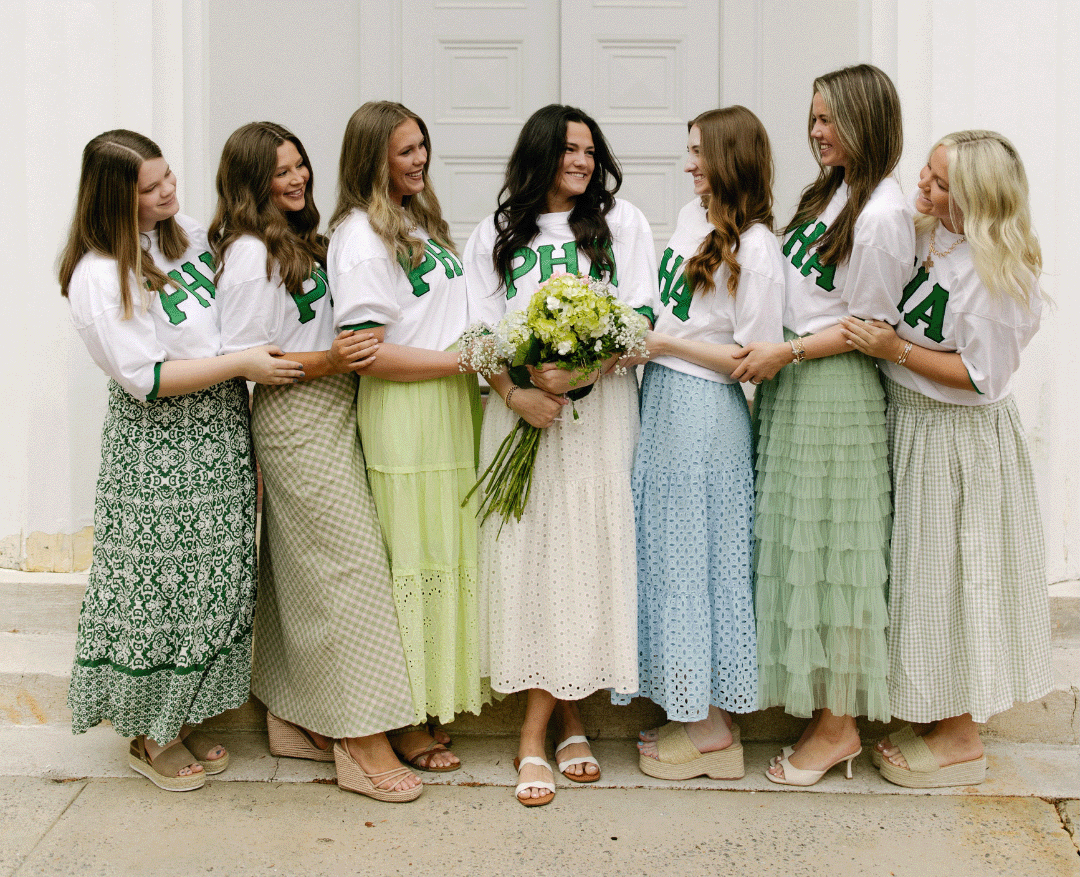 PHA executive members wearing white and green shirts with various shades of green skirts in front of a white building with middle girl holding flowers