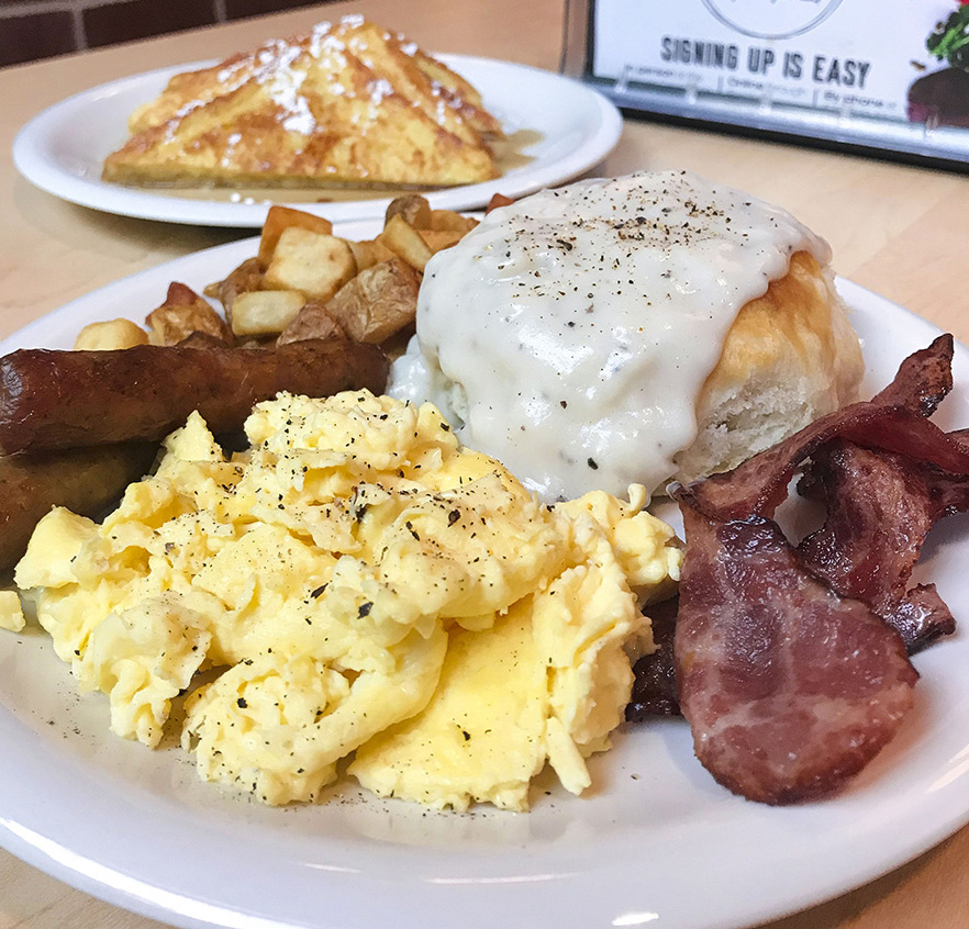 breakfast plate with biscuits and gravy, bacon, sausage, and eggs