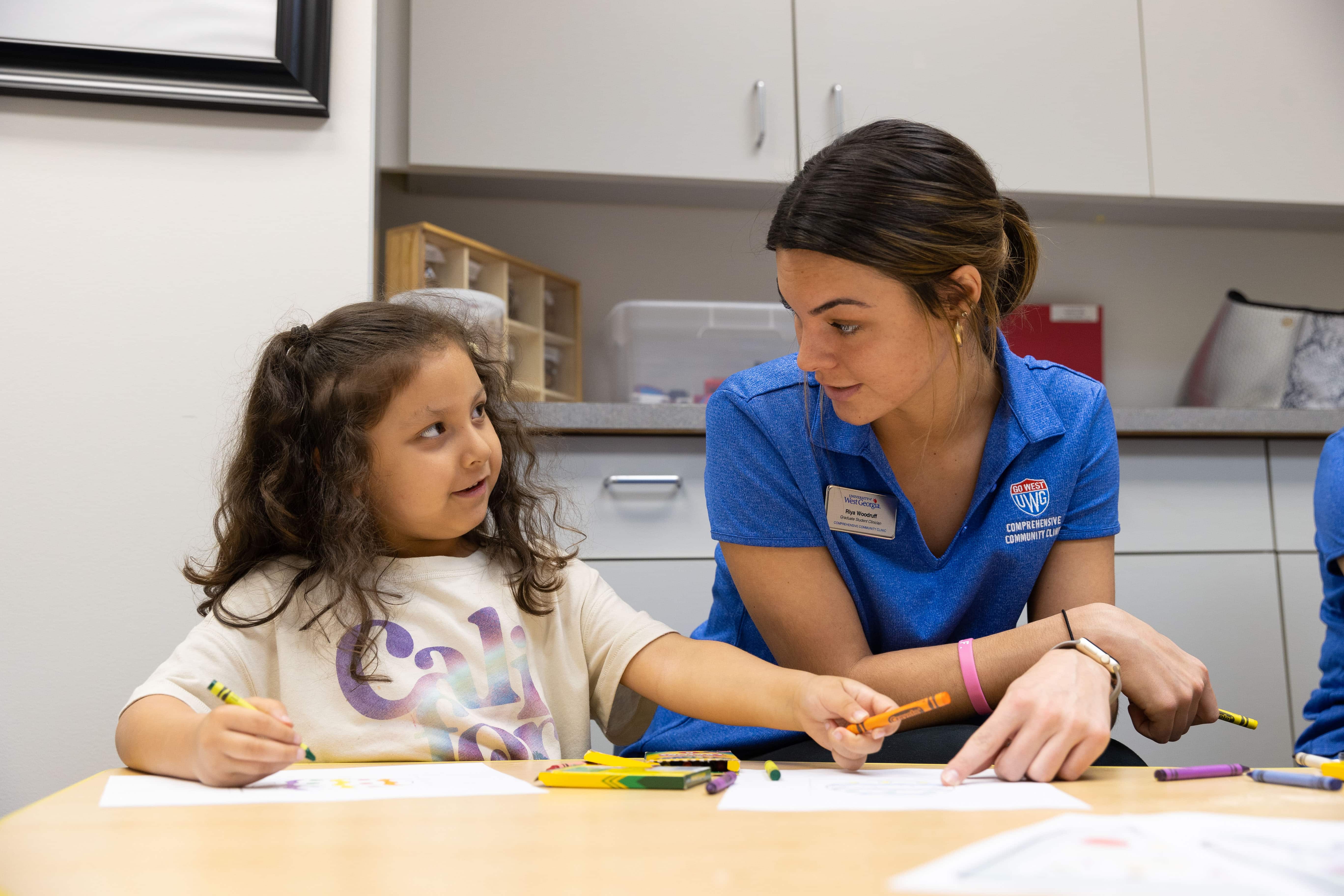 Early Learning Center teacher sitting with student using crayons.