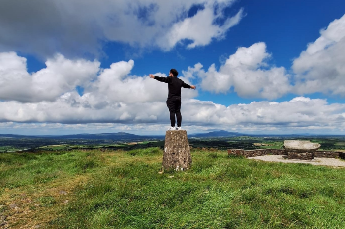 man standing on tree trunk in open field with arms extended