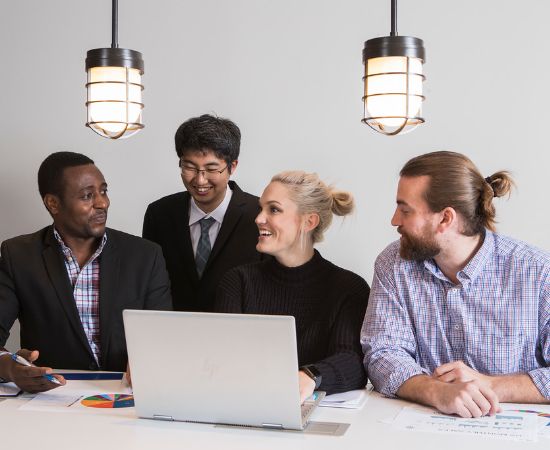 Four students in business attire working on a laptop