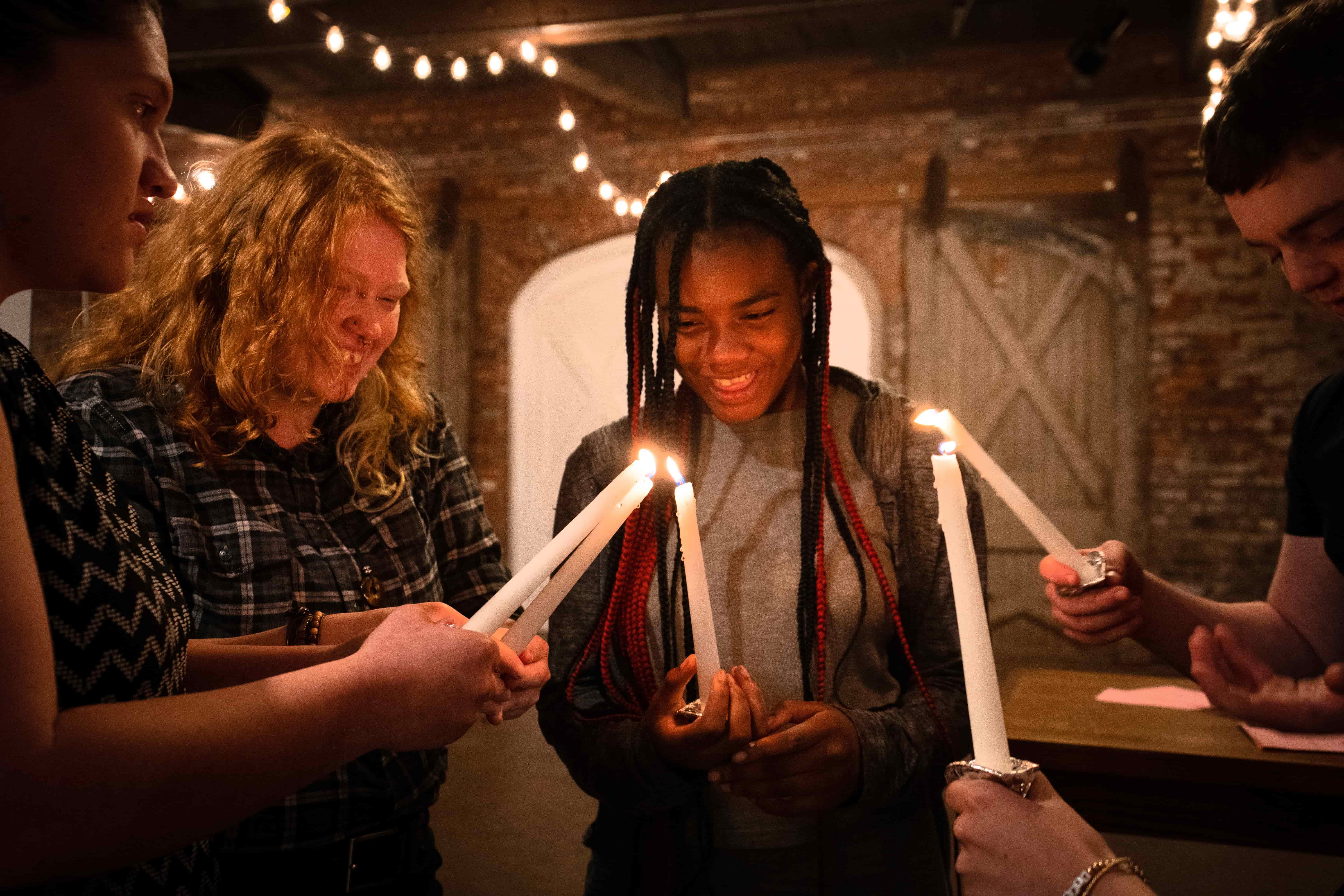 Students standing in a group holding lit candles, using one candle to light the others.