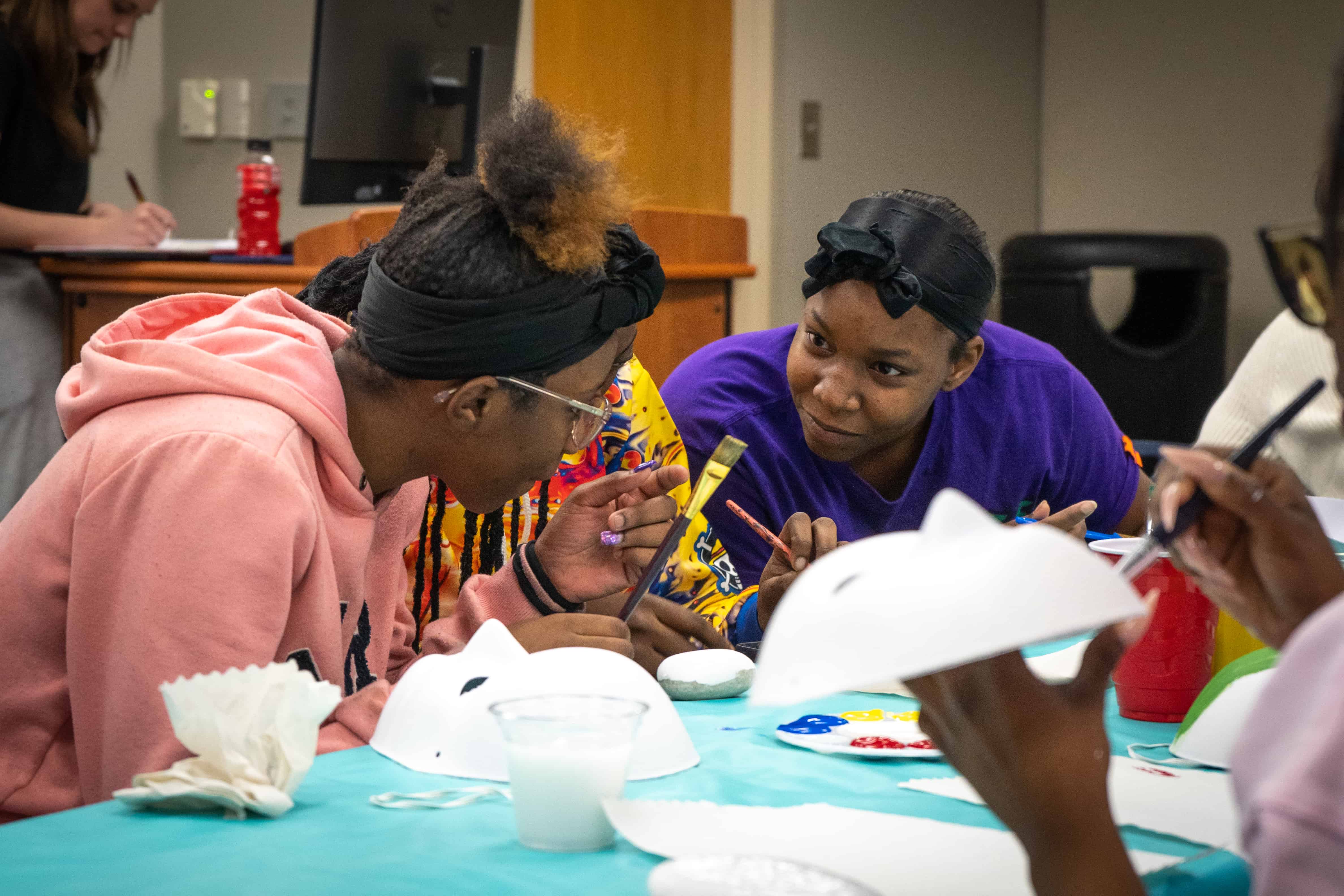 Students sitting together at a table painting on white masks.