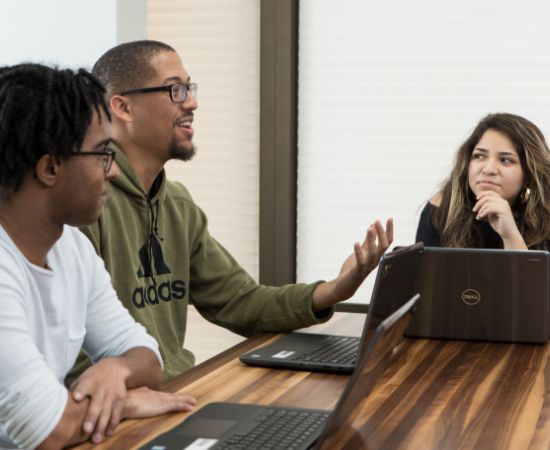 Students talking at a table with laptops