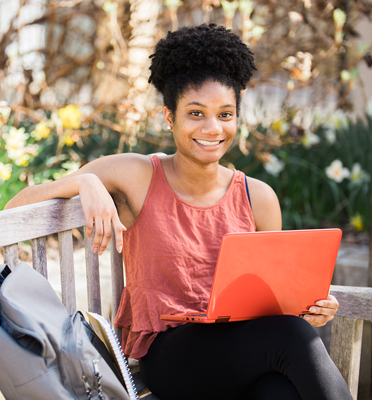 female student outside on bench with laptop