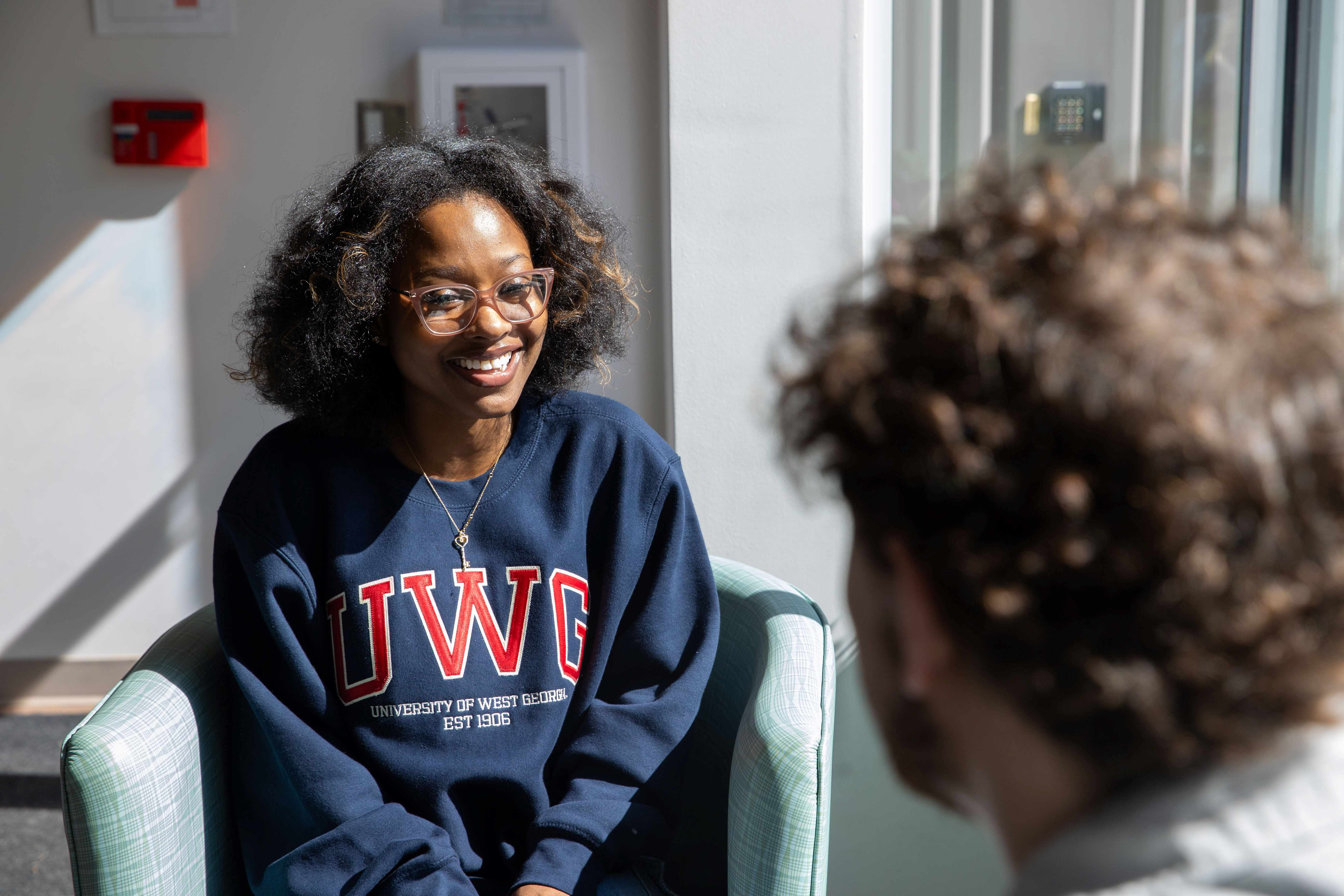 Girl student talking with a guy student while sitting in chairs across from each other.