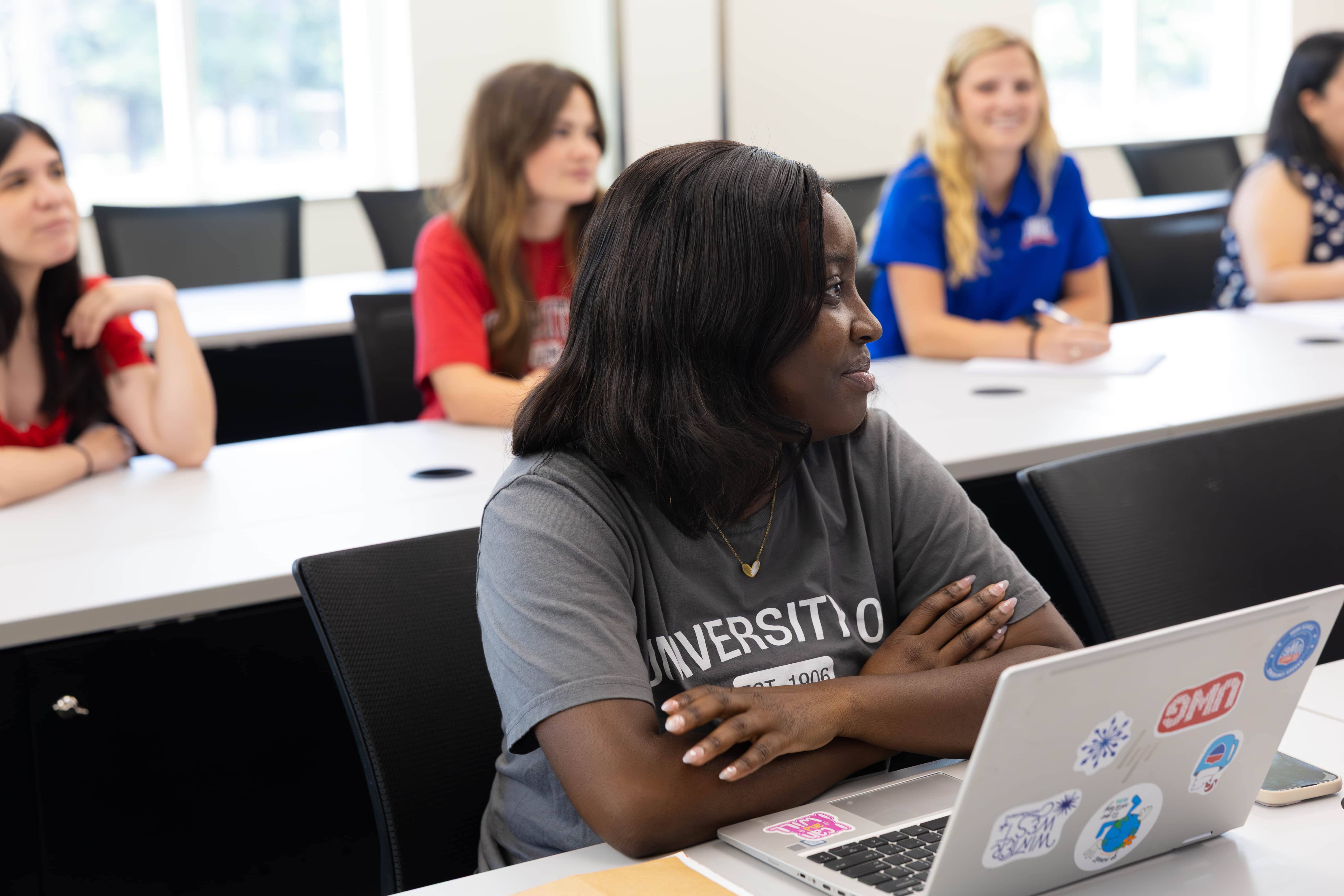 Student in a classroom smiling next to her laptop
