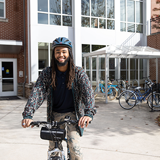 Student riding a bike in front of the Oaks. 