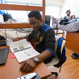 Student studying at a desk in a dorm room. 