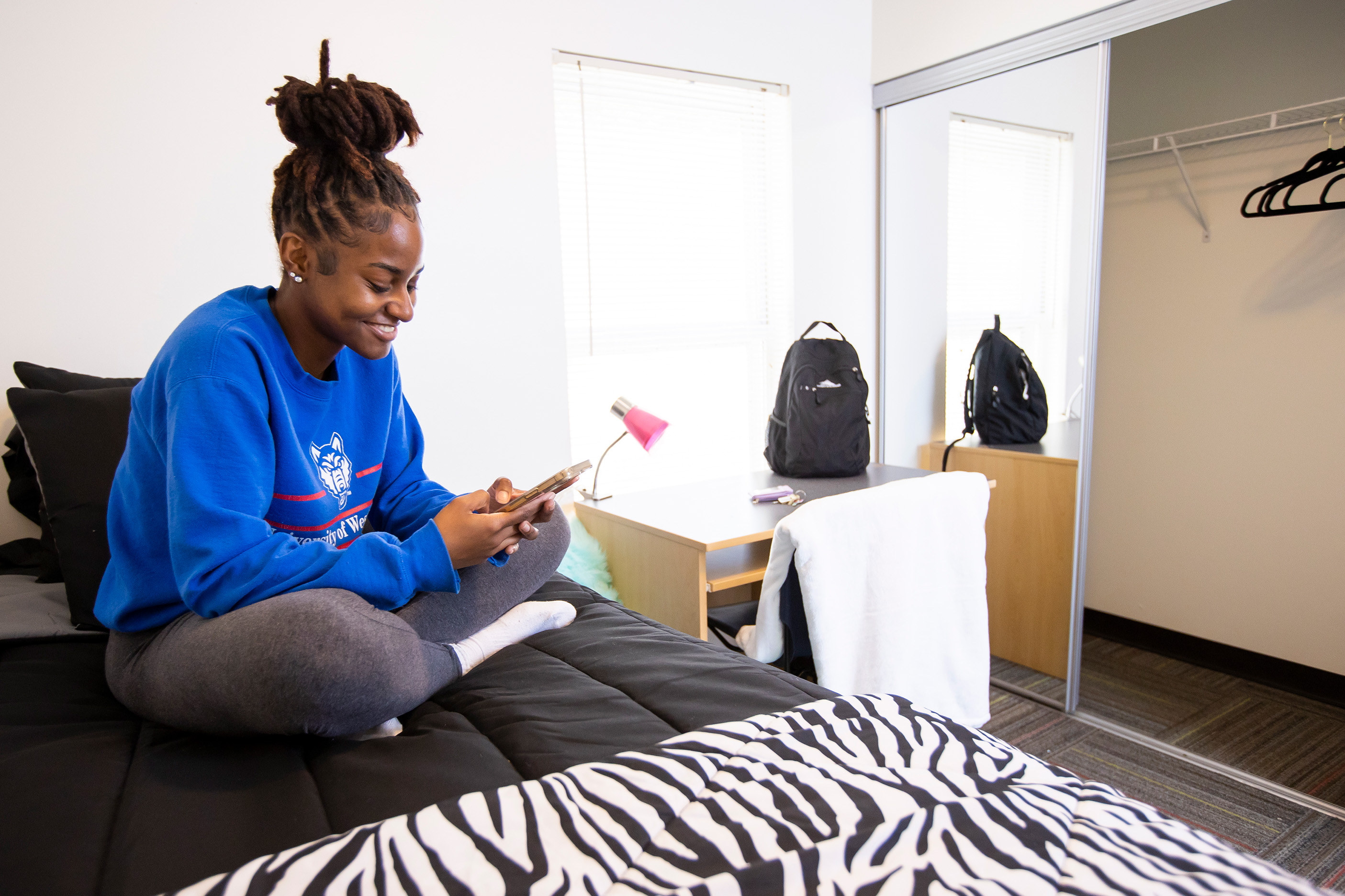 Student in private room looking at phone on bed