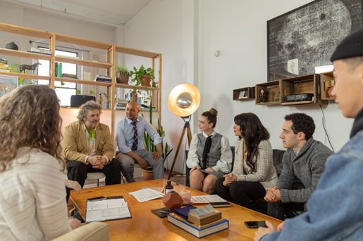 Photograph of a group of people meeting around a table with books and notepads.