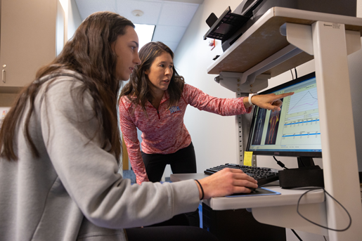 Photograph of an instructor pointing at a computer screen while working with a student.