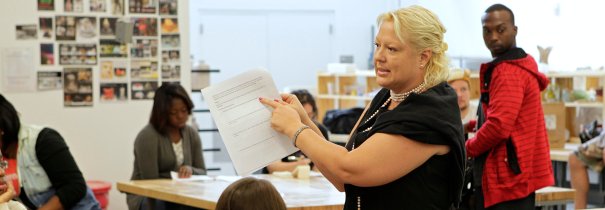 Lady holding up and pointing to a piece of paper in a classroom setting.