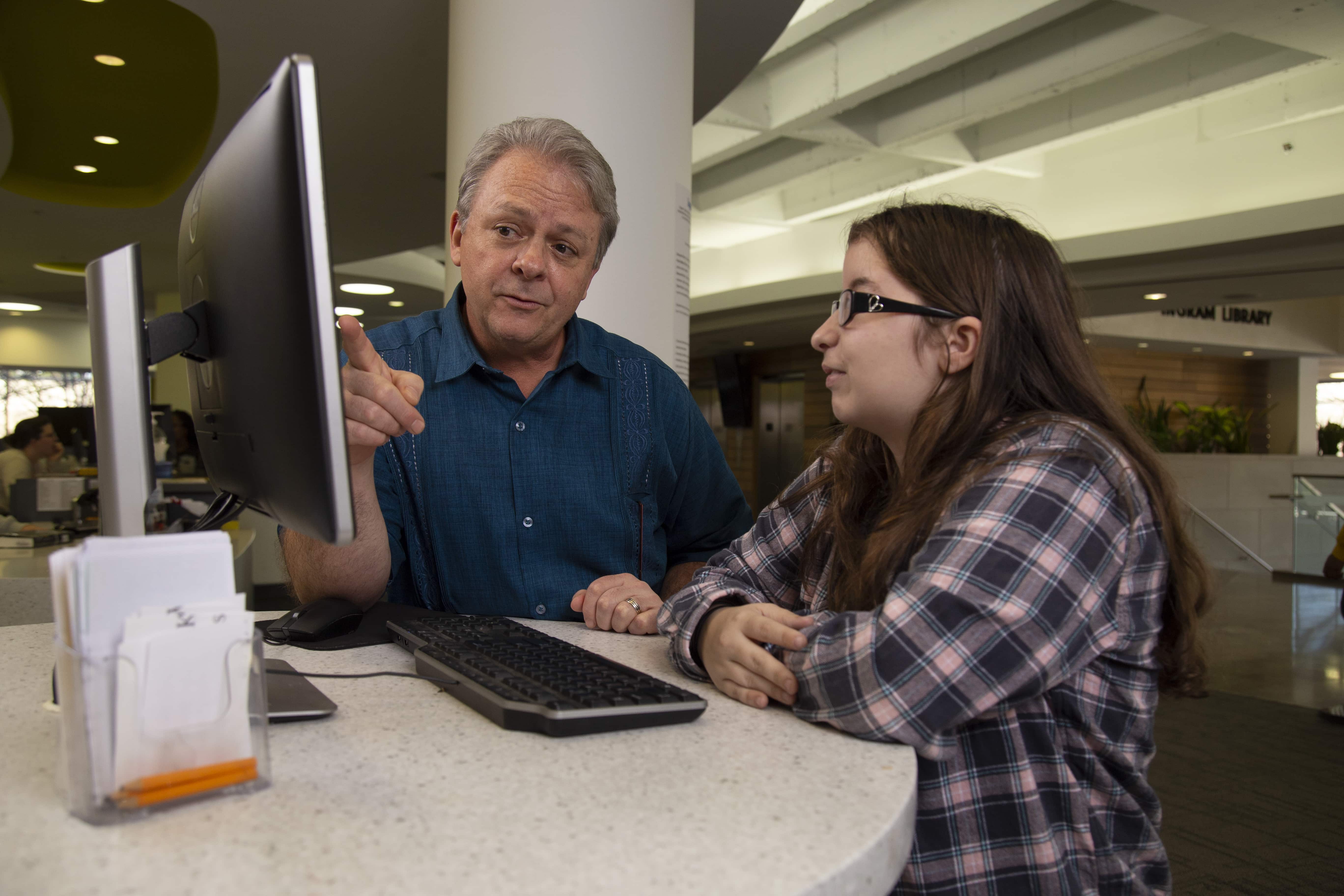 Library staff helping a student with a computer.
