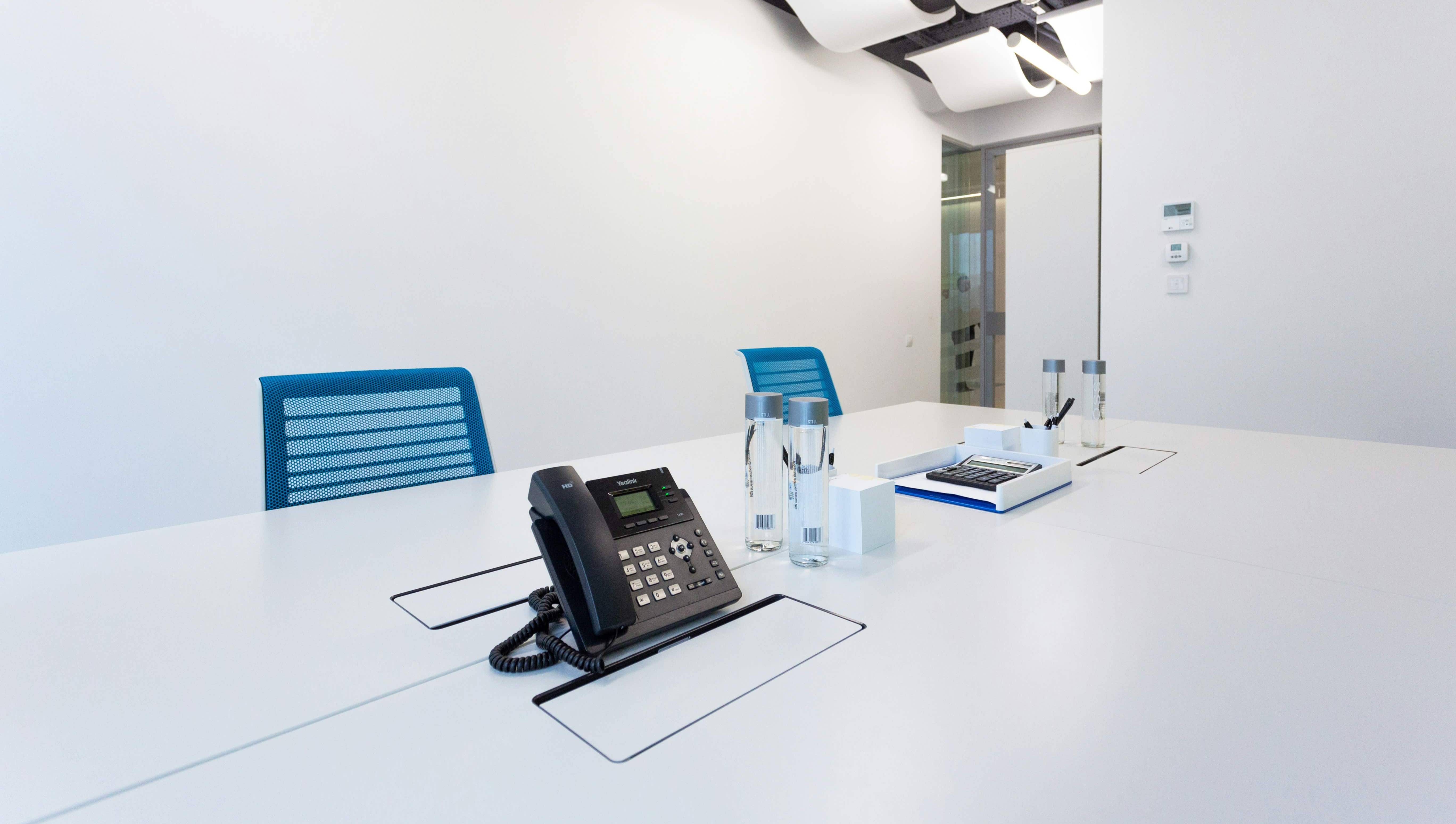 Meeting space with blue desk chairs, a conference table, and landline phone at the center of the table.