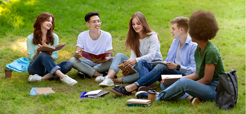 Students sitting outside in the grass reading books.
