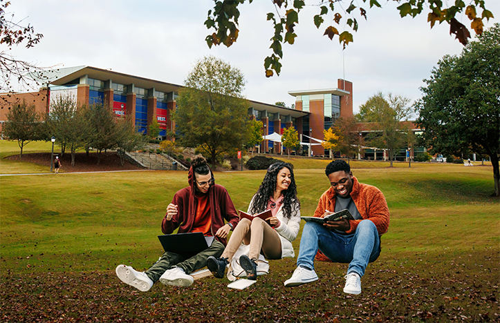 Three students sitting outside in the grass reading