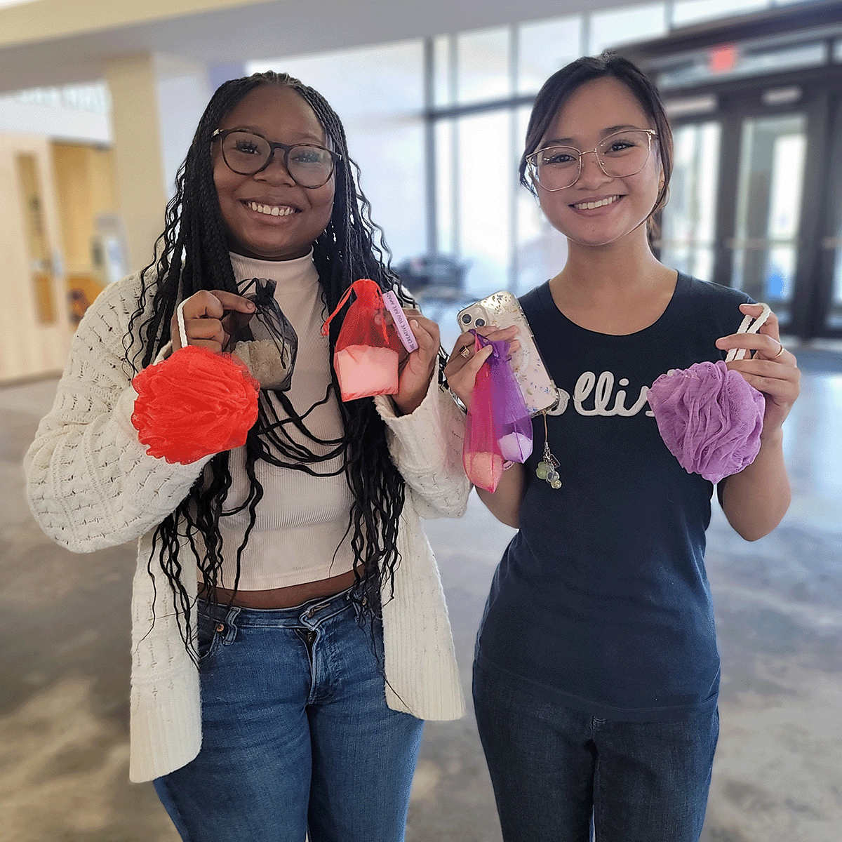 Two students smiling holding up some self care goodies from Spread Kindness