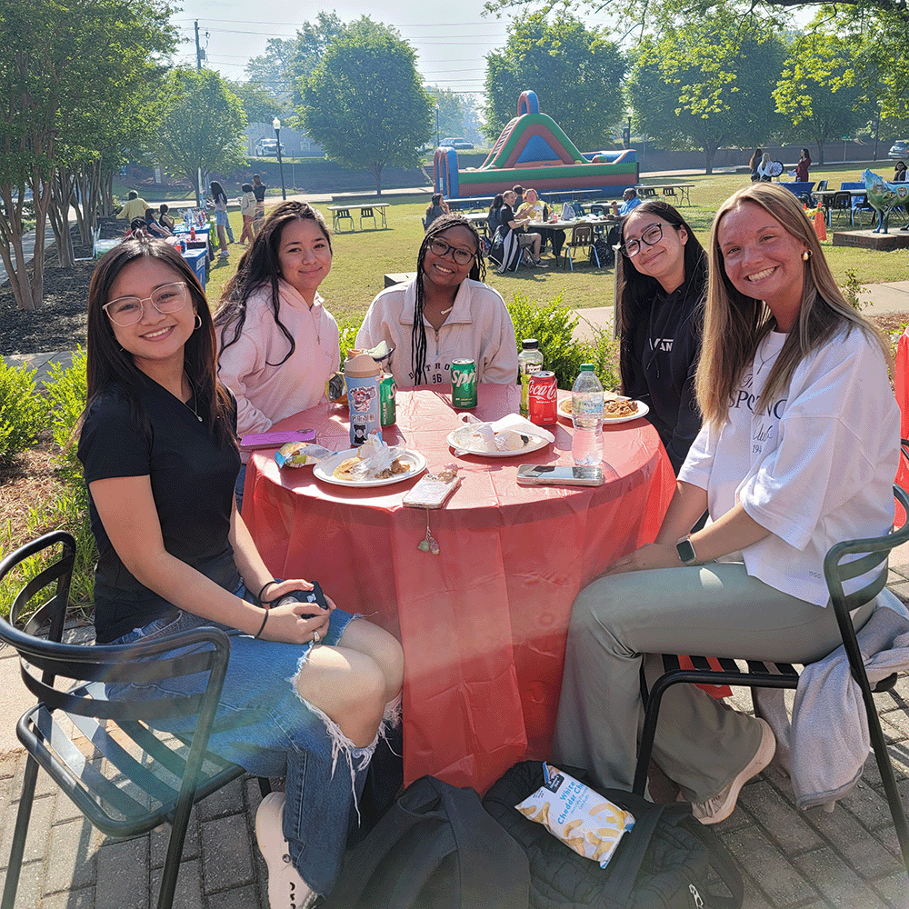 5 students smiling at a table outside at Welcome Wolves event on Newnan campus