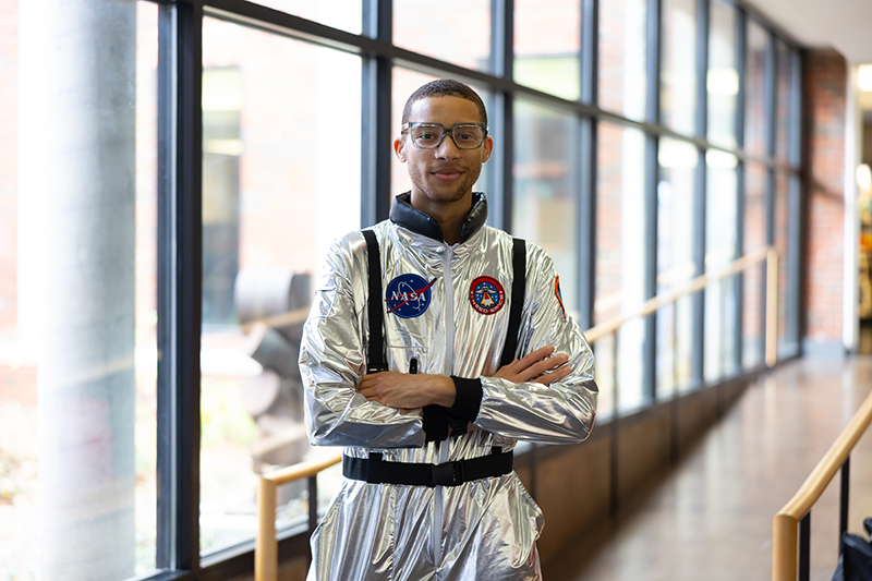 UWG student poses in silver space suit with a wall of windows behind him