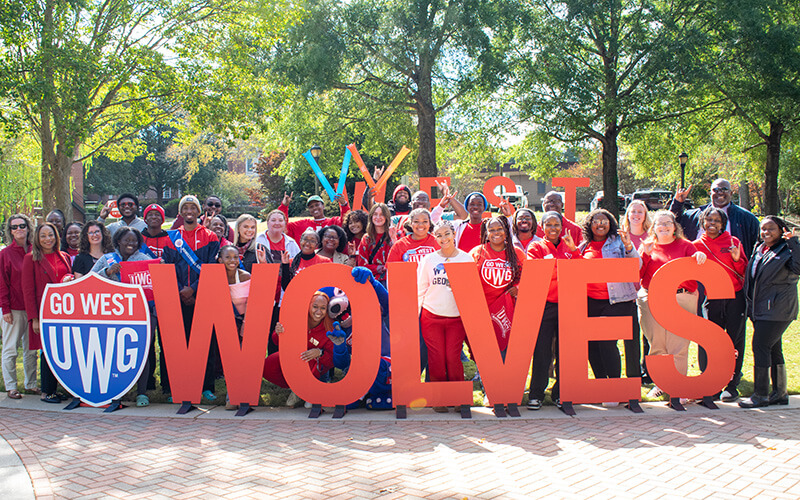 UWG faculty, staff and students stand behind a red Wolves sign