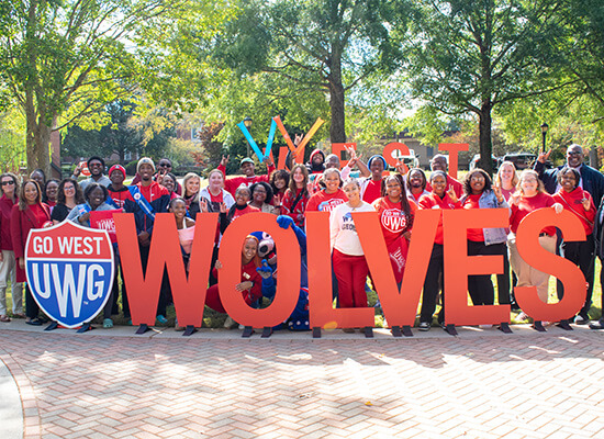 UWG faculty, staff and students stand behind a Wolves sign during Homecoming 2023
