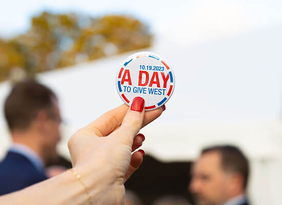 Person holding a sticker that reads "10.19.23: A Day to Give West"